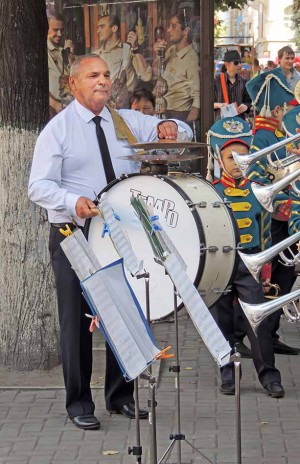Mature man playing the bass drum in the brass band composition on the city street during the celebration of the City Day