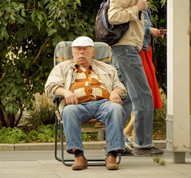 Senior adult man slumbering in a chair on the street sidewalk