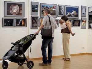 Family with elementary age girl and pram in a gallery. Classic Photo Gallery. Russian Week Of Photography 2016